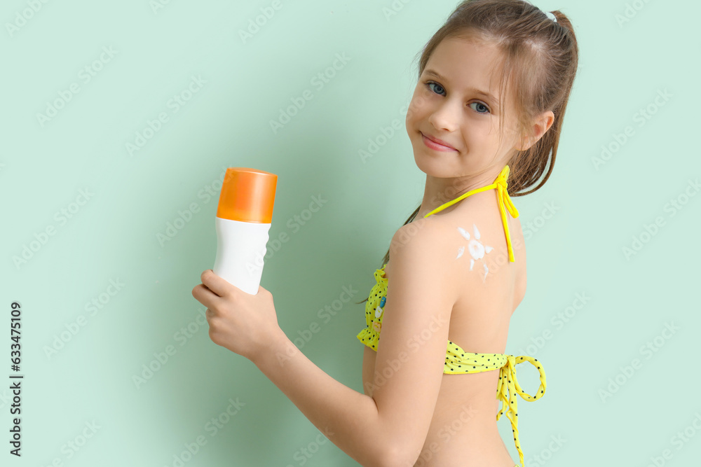 Little girl with bottle of sunscreen cream on pale green background