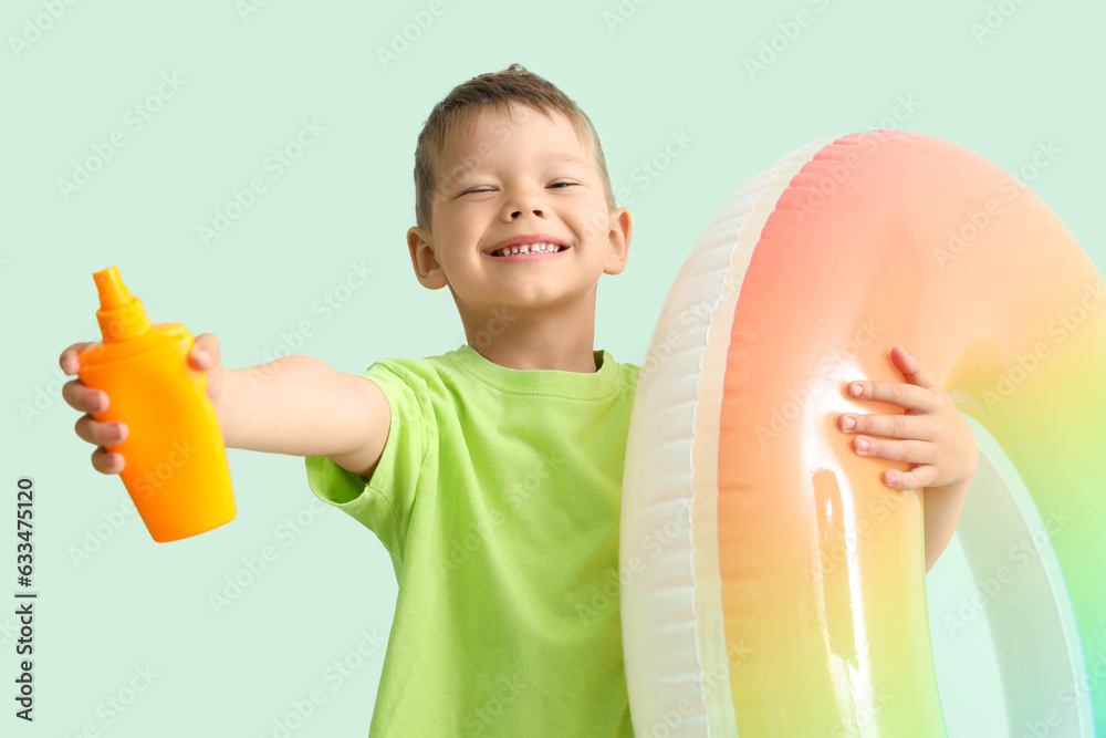 Little boy with bottle of sunscreen cream and inflatable ring on pale green background