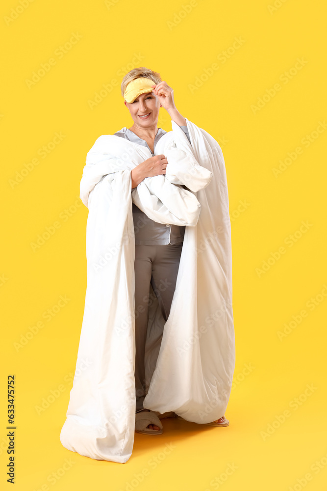 Mature woman in sleeping mask with blanket on yellow background