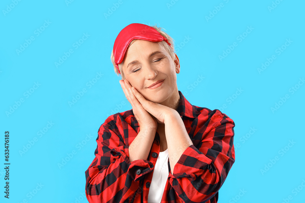 Mature woman in pajamas and sleeping mask on blue background, closeup