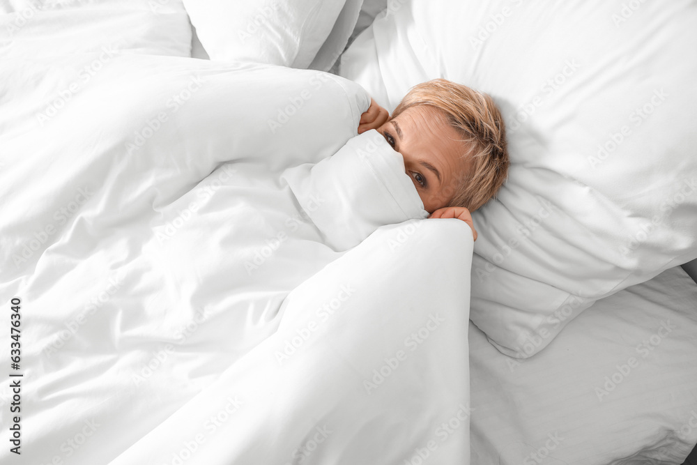 Mature woman lying under blanket in bed