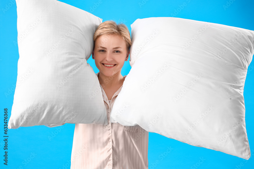 Young woman in pajamas with pillows on blue background