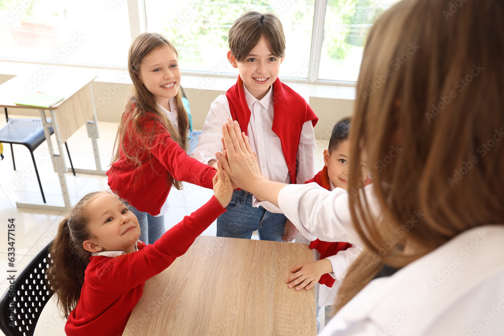 Little pupils with their teacher putting hands together in classroom