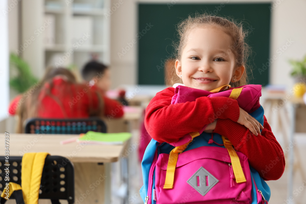 Cute little schoolgirl with backpack in classroom