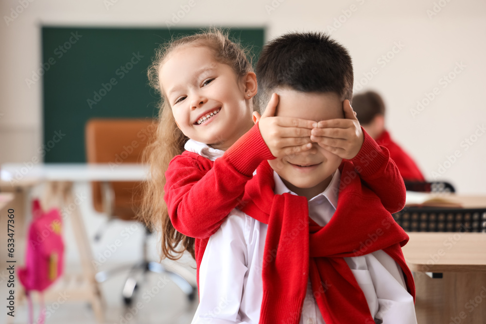 Little girl closing her classmates eyes in classroom