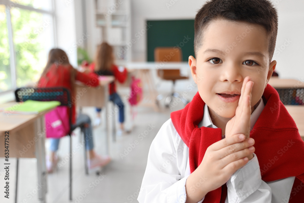 Cute little schoolboy whispering in classroom, closeup