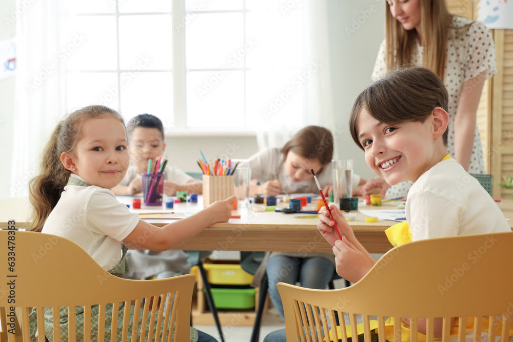 Little pupils drawing with teacher in art class