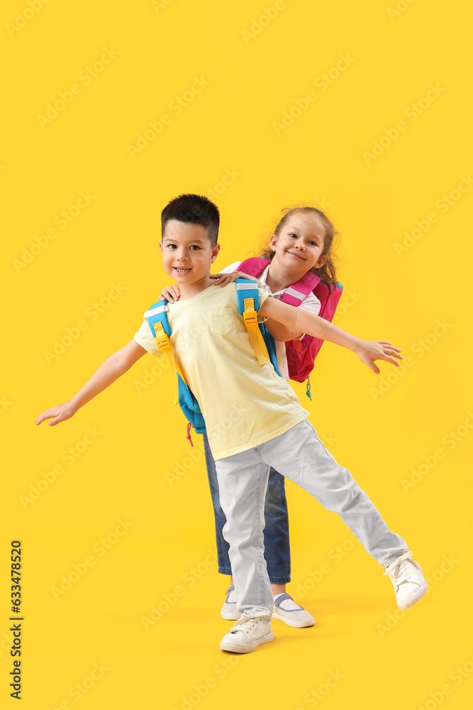 Cute little pupils with backpacks on yellow background