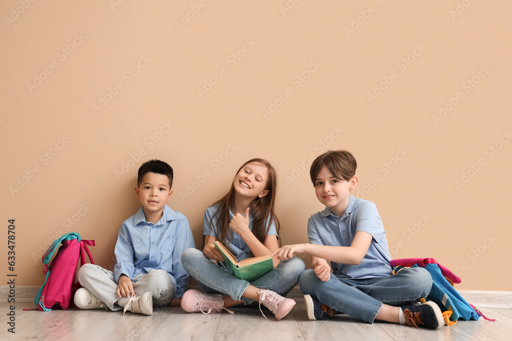 Little pupils reading book near beige wall