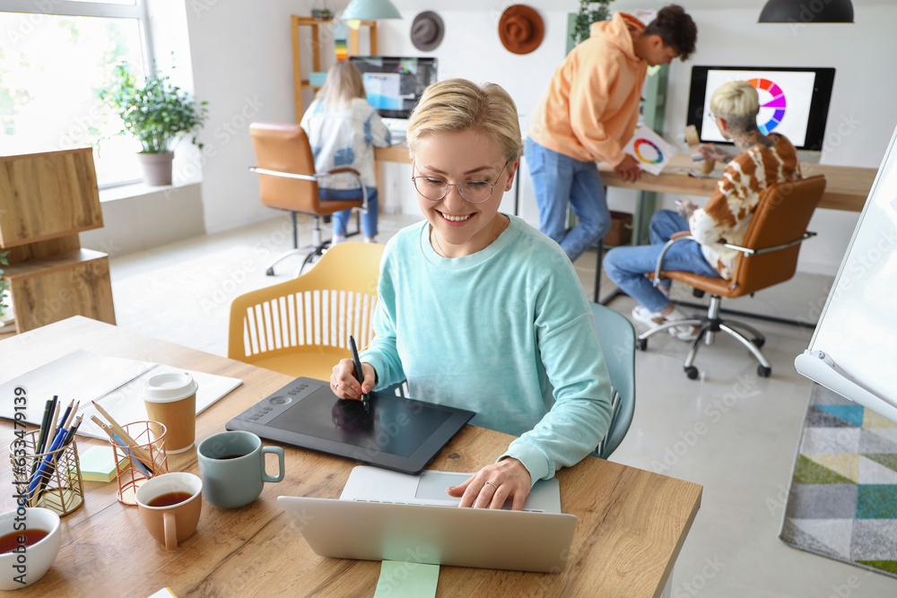 Female graphic designer working with tablet and laptop at table in office