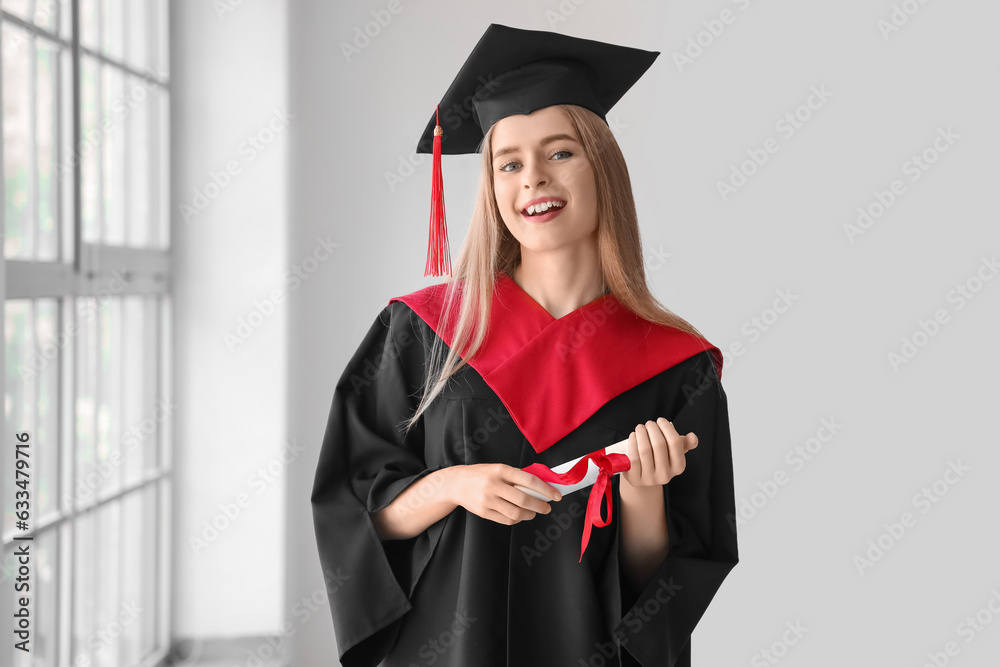 Female graduate student with diploma near window in room