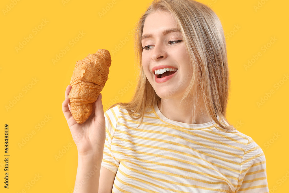 Young woman with tasty croissant on yellow background, closeup