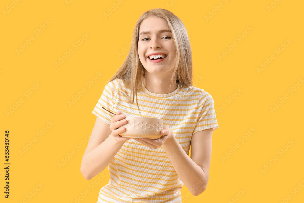 Young woman with bowl and spoon on yellow background