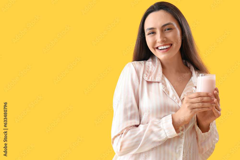 Young woman in pajamas with tasty yoghurt on yellow background