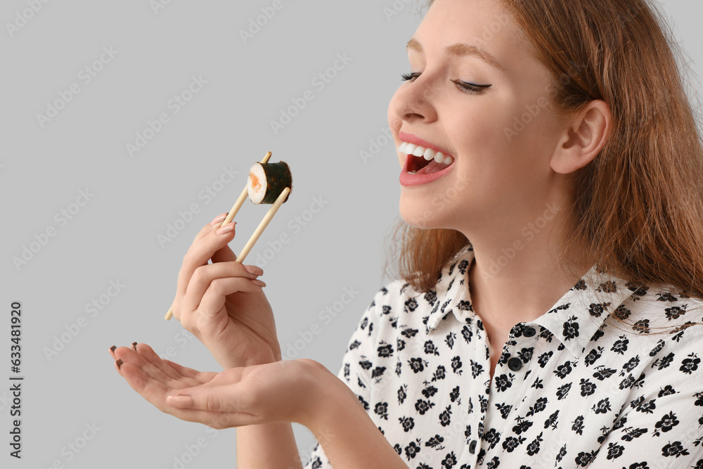 Young woman with tasty sushi roll on grey background, closeup