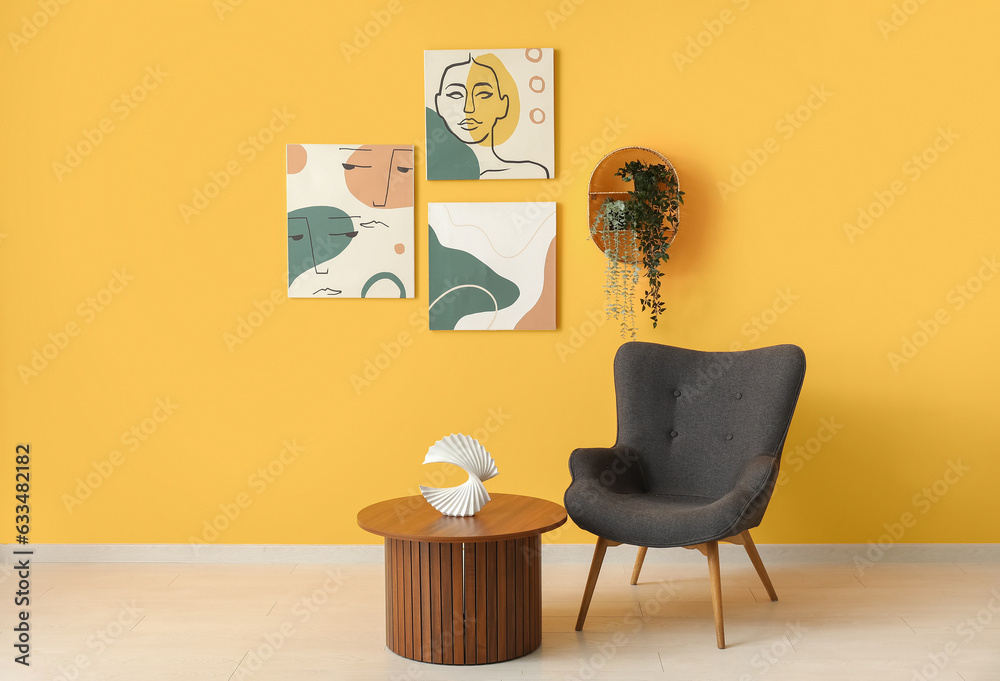 Grey armchair and wooden coffee table near orange wall with different paintings