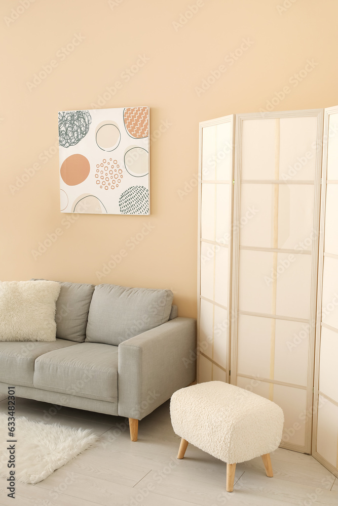 Interior of living room with grey sofa, folding screen and painting