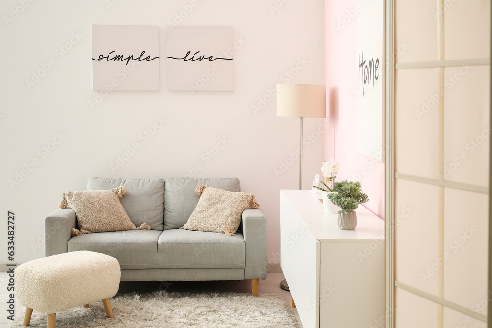 Interior of living room with cozy grey sofa, white cabinet and posters