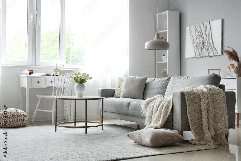 Cozy grey sofa with soft blanket and table in interior of light living room