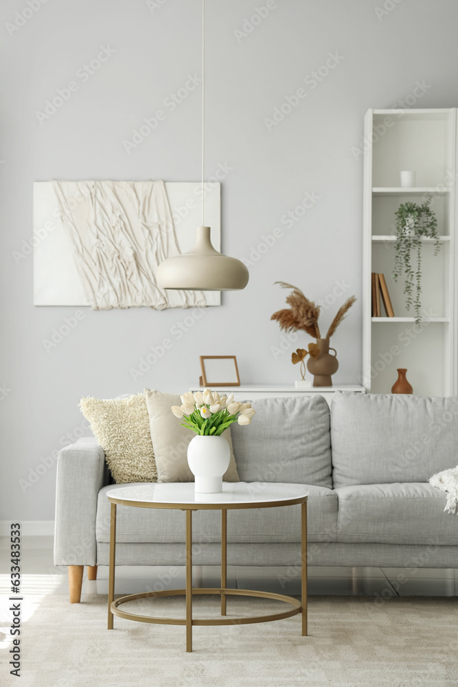 Cozy grey sofa and vase with tulip flowers on coffee table in interior of living room