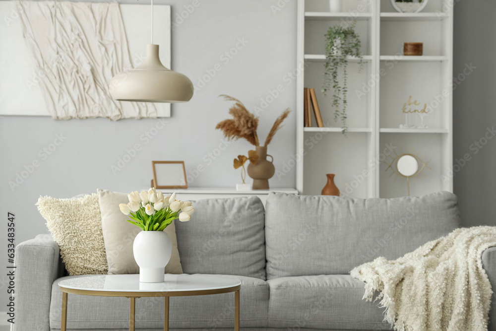 Cozy grey sofa with soft blanket and coffee table in interior of light living room