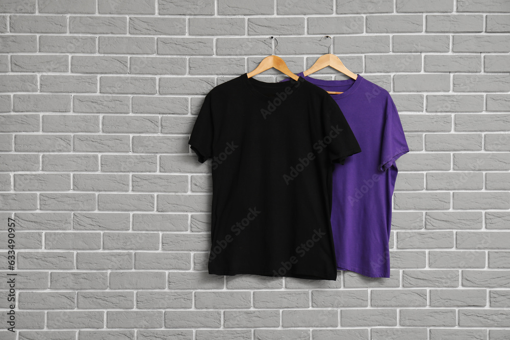 Stylish t-shirts hanging on grey brick wall