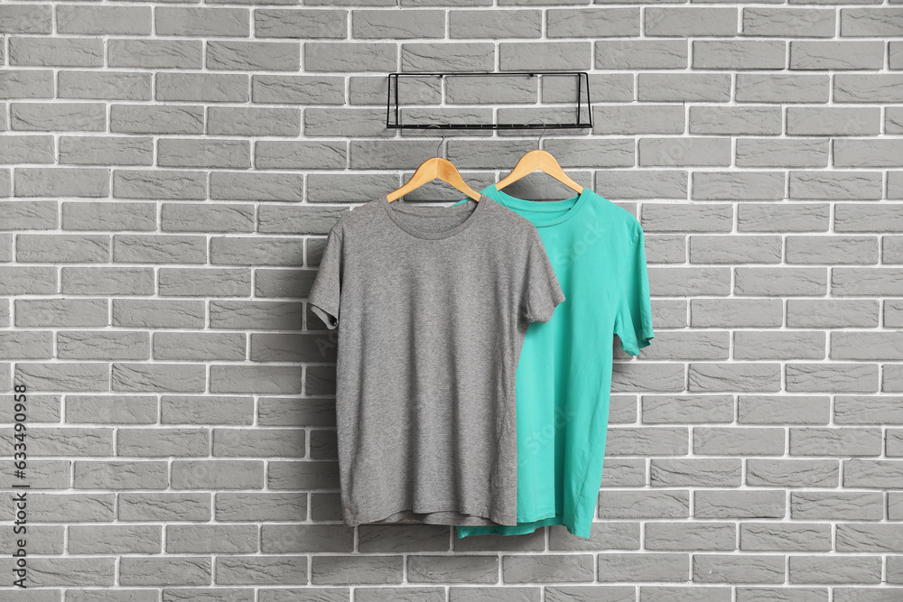 Stylish t-shirts hanging on grey brick wall