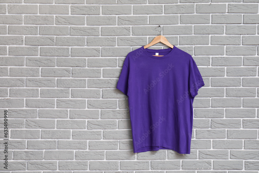 Stylish purple t-shirt hanging on grey brick wall