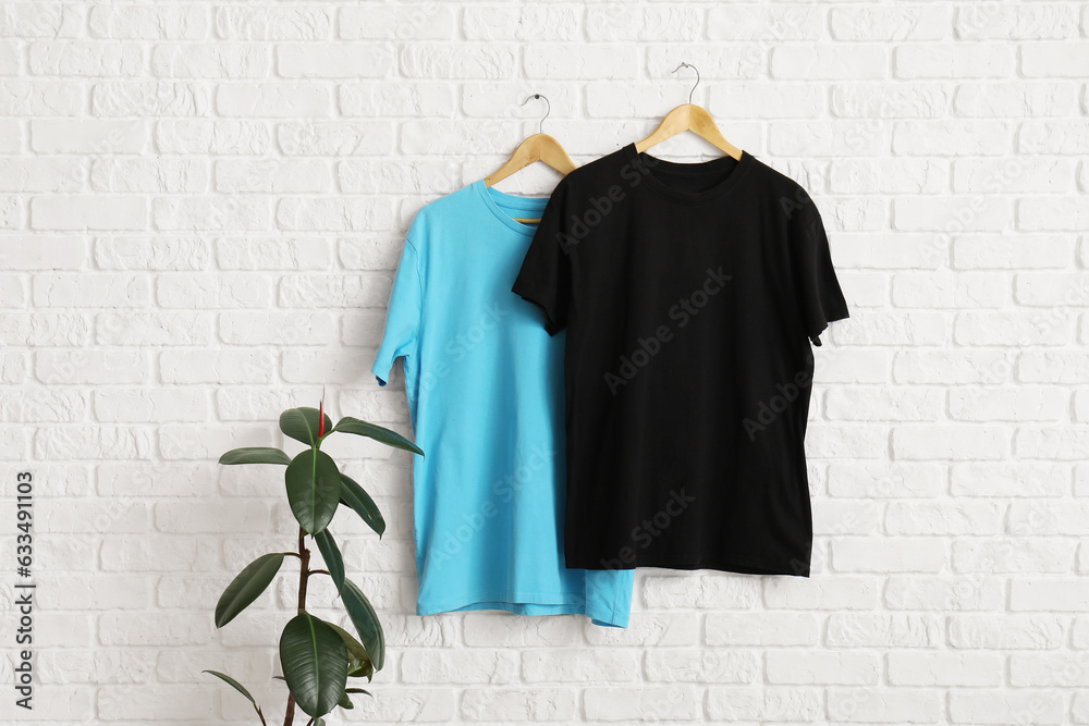 Stylish t-shirts hanging on white brick wall