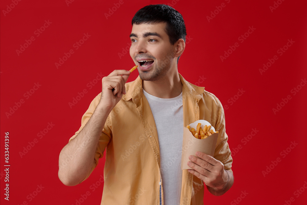 Young man eating french fries on red background