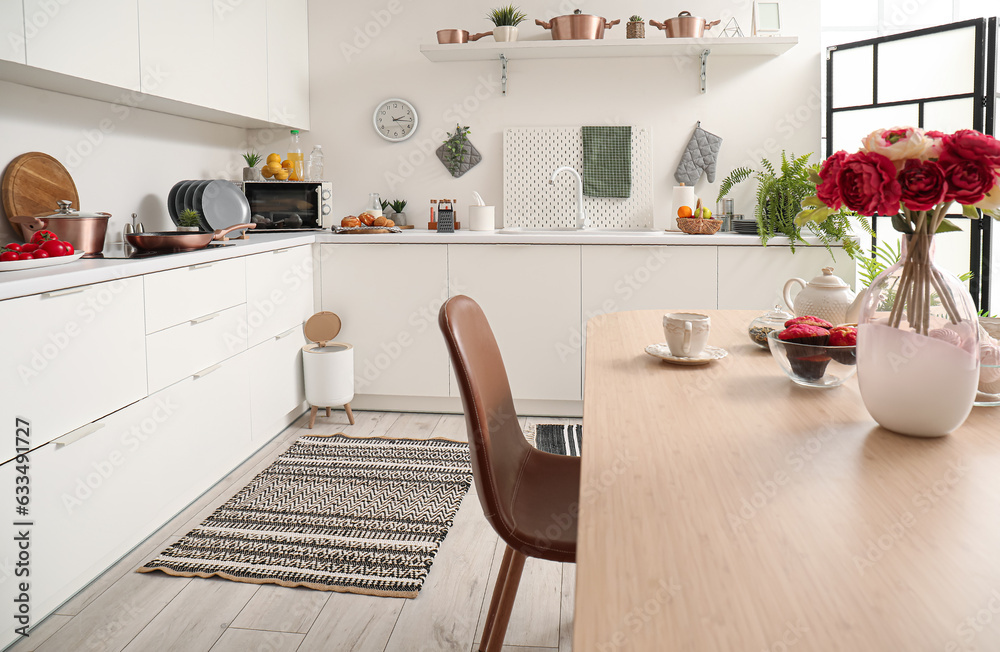 Interior of modern kitchen with dining table, stylish rug and trash bin