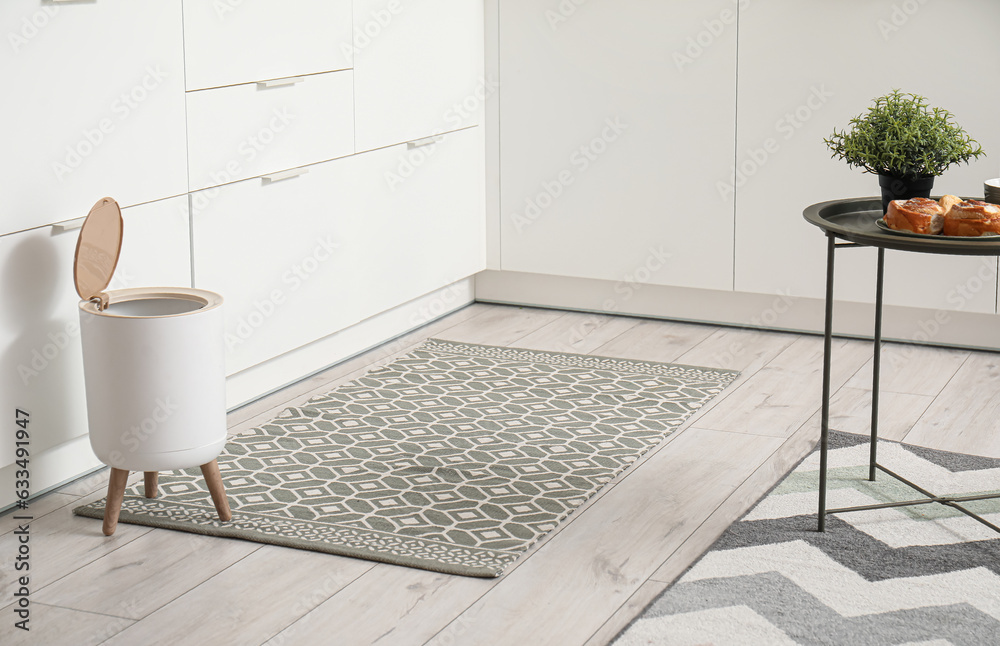 Interior of modern kitchen with stylish rug, trash bin and white counters