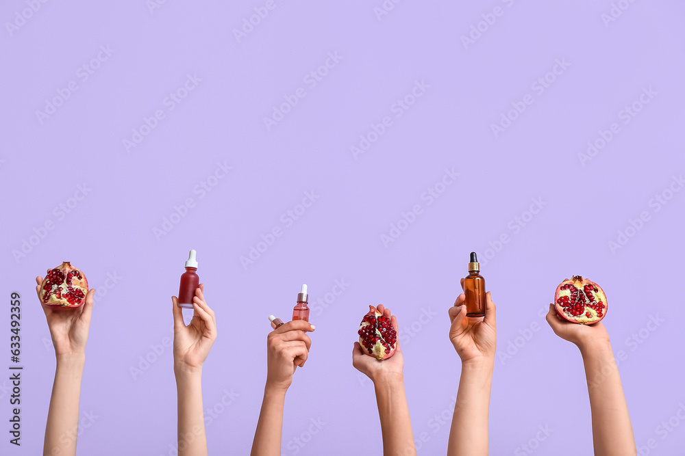 Female hands holding cosmetic products and pomegranate on lilac background