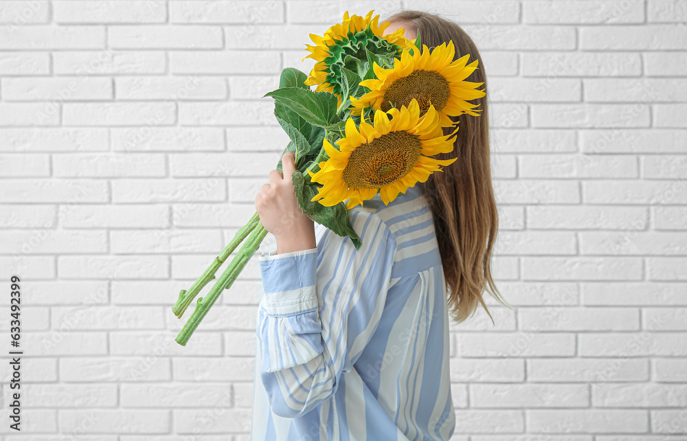 Woman with beautiful sunflowers on light brick background