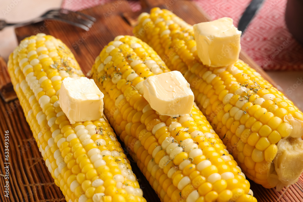 Wooden board of boiled corn cobs with butter on table, closeup