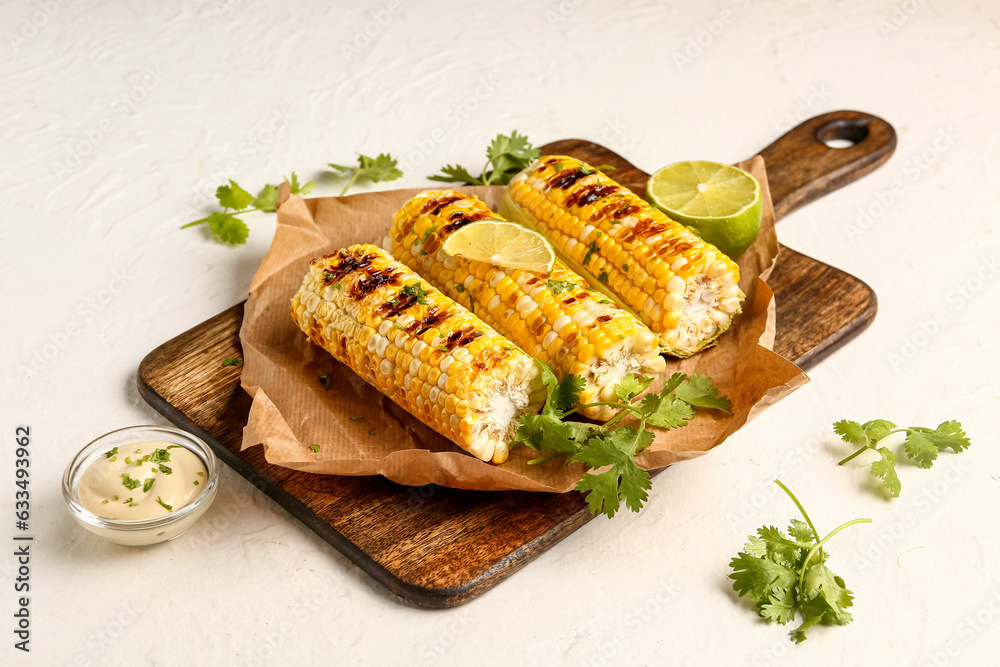 Baking paper with tasty grilled corn cobs and lime on white background