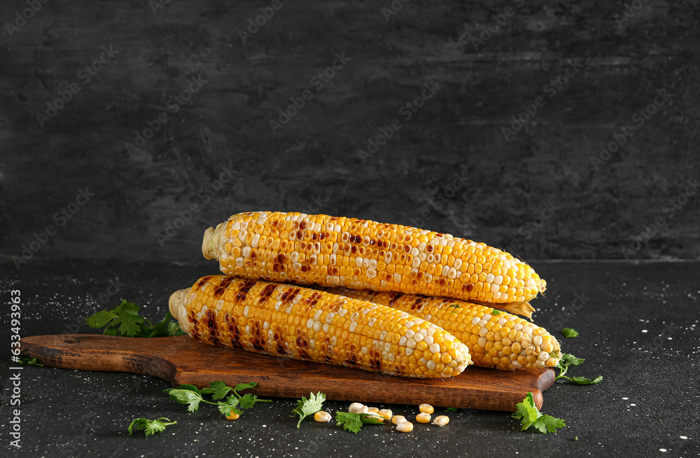 Wooden board with tasty grilled corn cobs and parsley on black background