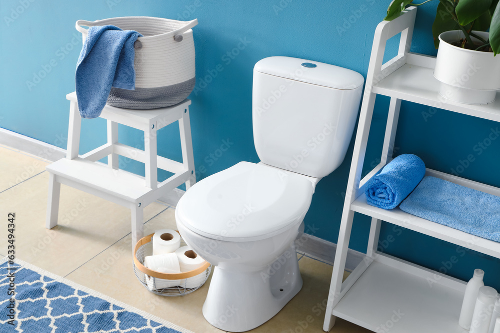 Interior of modern restroom with ceramic toilet bowl and shelving unit near blue wall