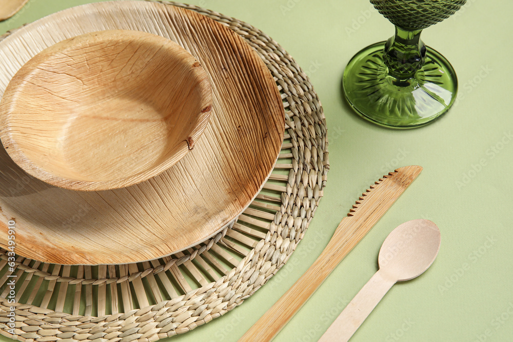 Different wooden tableware and glass on green background, closeup