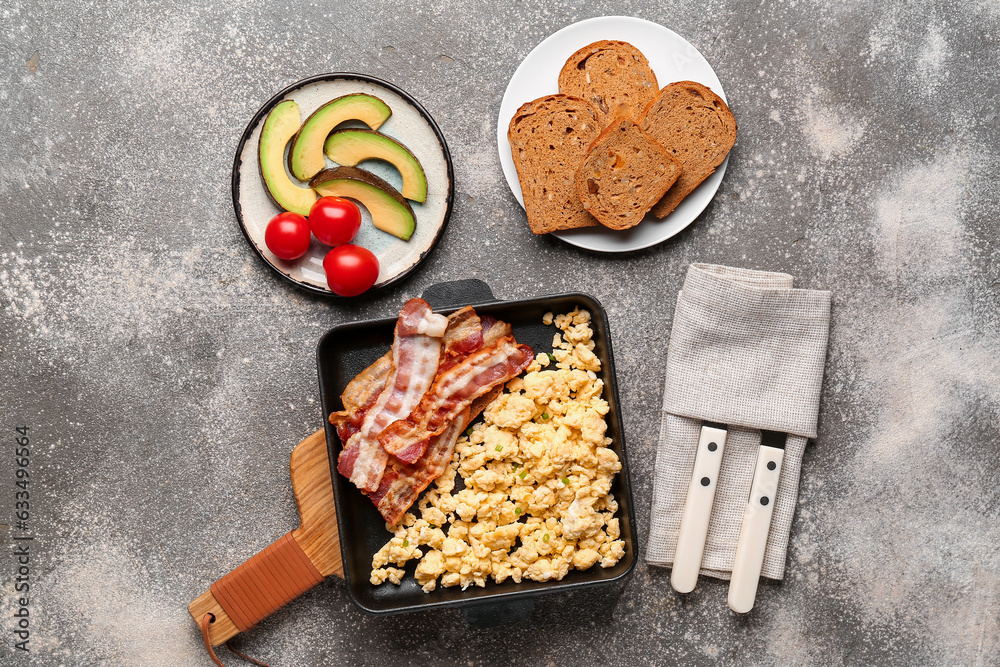 Frying pan of tasty scrambled eggs with bacon on grey background