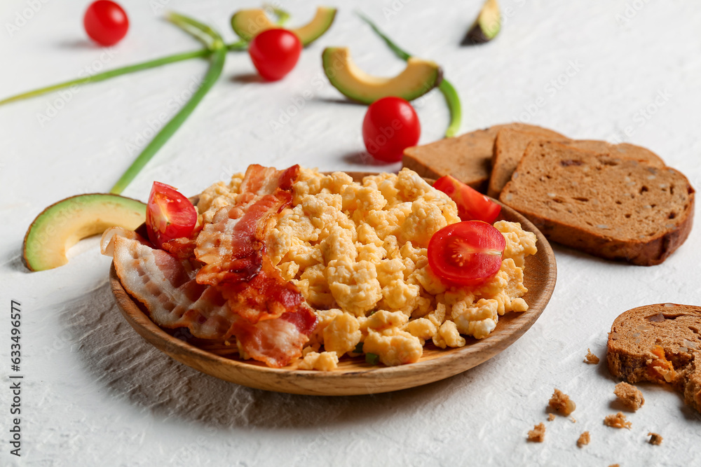 Plate of tasty scrambled eggs with bacon on white background