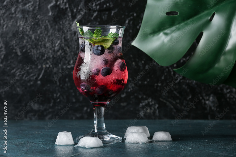 Glass of fresh blueberry lemonade with mint and monstera leaf on dark table