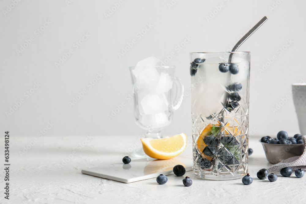 Glass of fresh blueberry lemonade and bowl with berries on white background