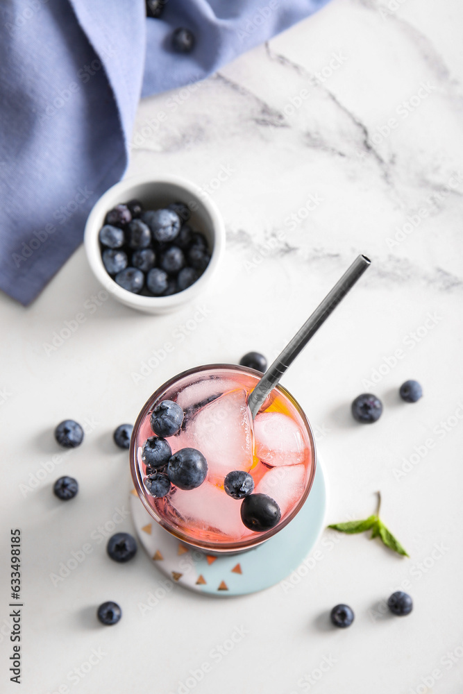 Glass of fresh blueberry lemonade and bowl with berries on white background