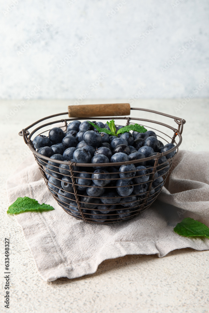 Basket with fresh blueberries and mint on white background