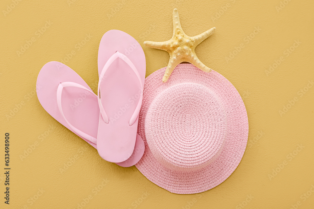 Pair of pink flip flops with hat and starfish on beige background