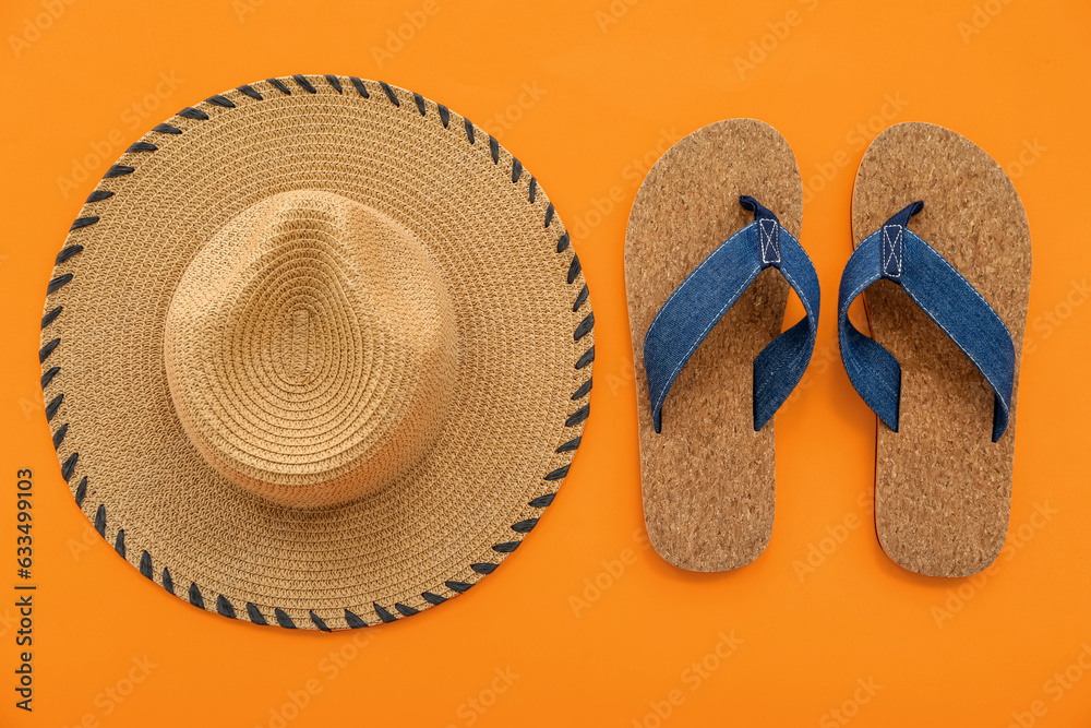 Pair of flip flops and straw hat on orange background