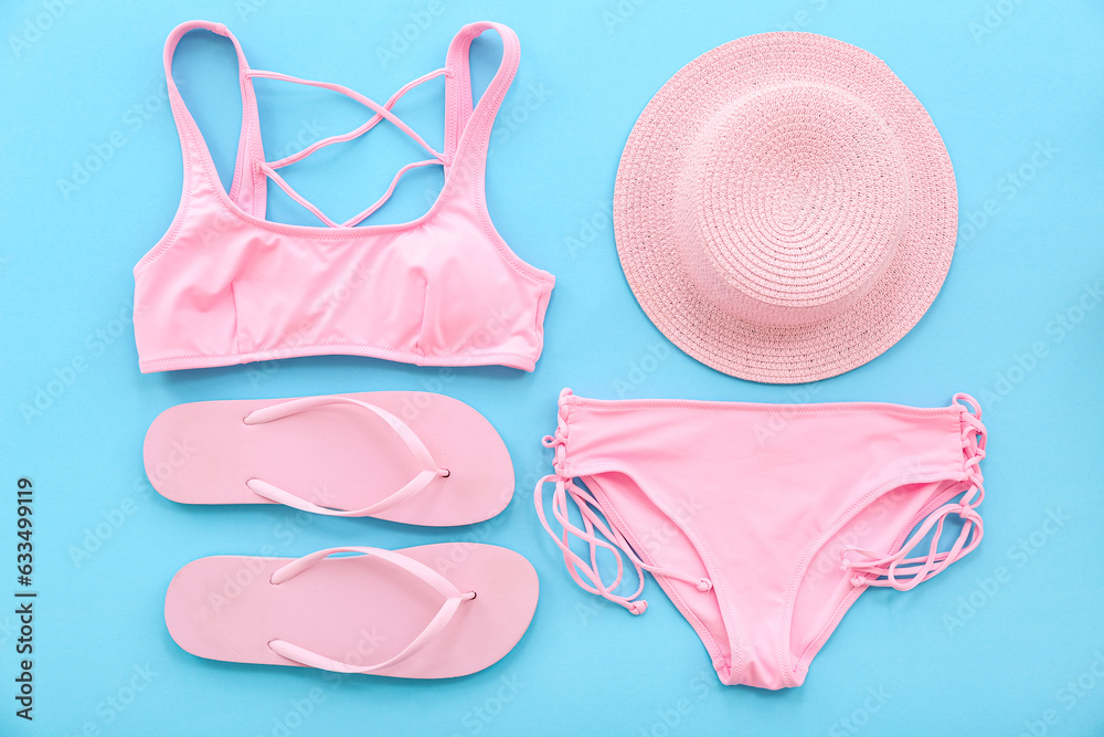 Pair of pink flip flops with swimsuit and hat on blue background