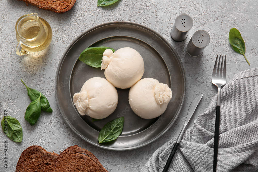 Plate of tasty Burrata cheese with basil and bread on grey table