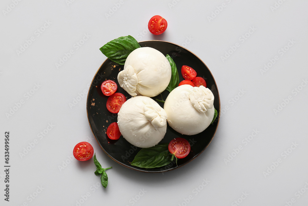 Plate of tasty Burrata cheese with basil and tomatoes on white background